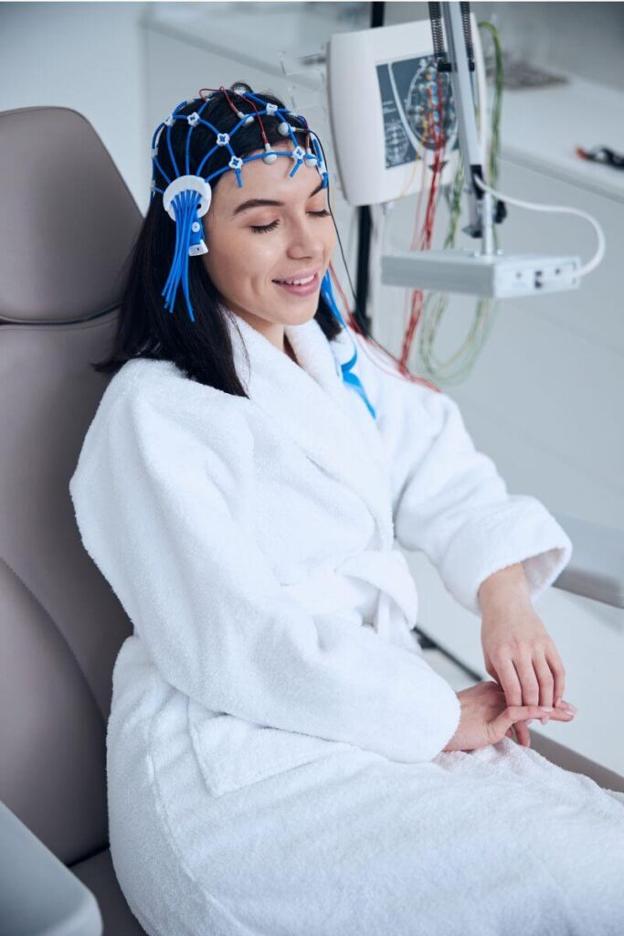 Brain EEG at Your Health In Motion - A woman is relaxing in chair, wearing a fluffy white robe, and an electrode cap on her head.