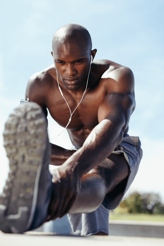 A bald, shirtless black man stretching out his leg